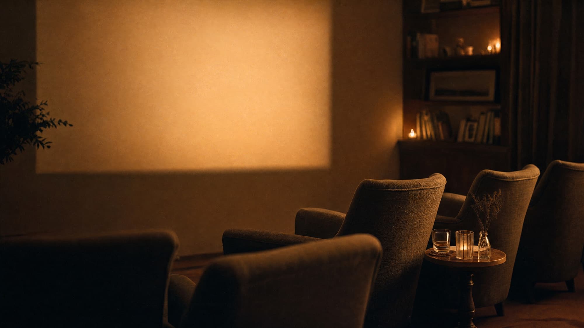A warm, candlelit room with armchairs facing a softly lit screen